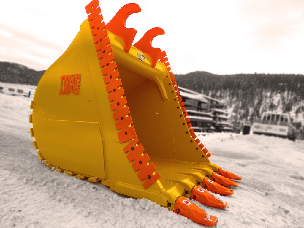 Excavator dig bucket manufactured by Tysea Mfg.  Painted yellow with replaceable pin on teeth and bolt on serrated cutting edges
