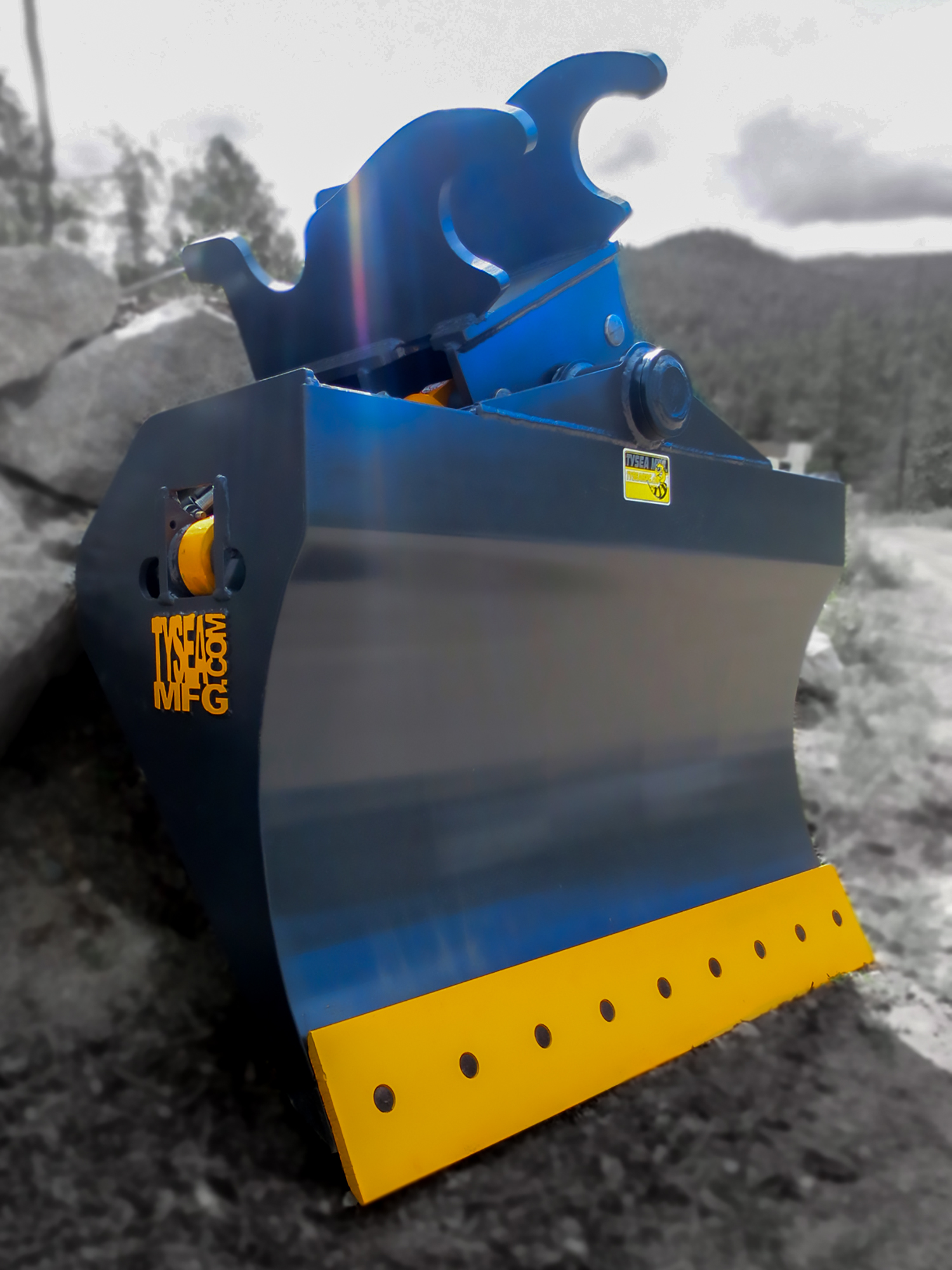 Grey and yellow excavator chuck blade, featuring smooth bolt on cutting edge and tilting design with dual hydraulic cylinders.