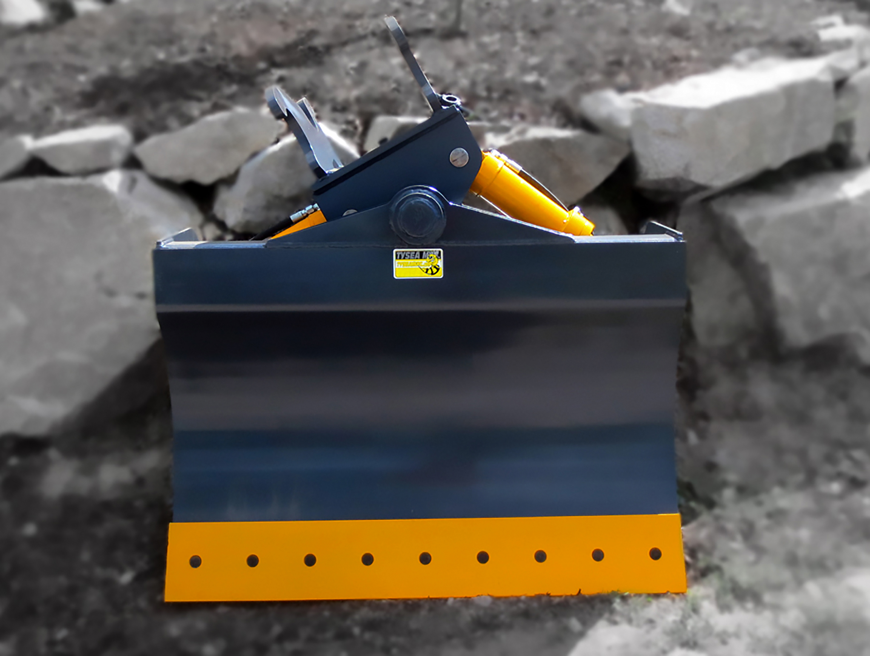 Grey and yellow excavator chuck blade, featuring smooth bolt on cutting edge and tilting design with dual hydraulic cylinders.