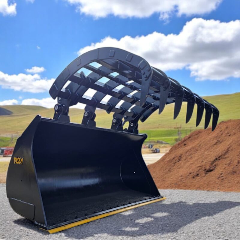 Wheel loader grapple bucket in gravel lot with dirt piles