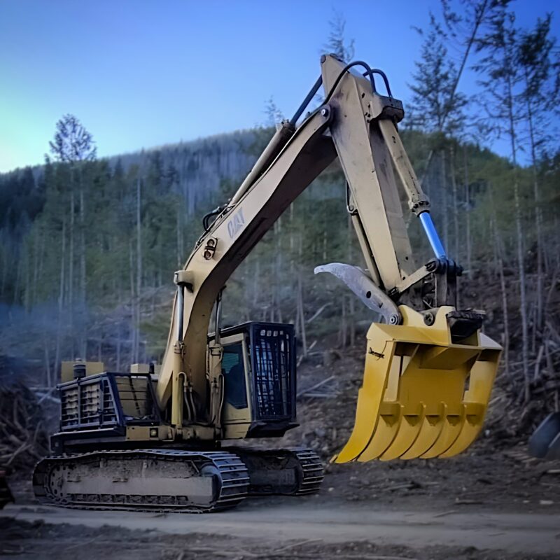CAT excavator with 400 Series brush rake clearing brush and debris in a forested area